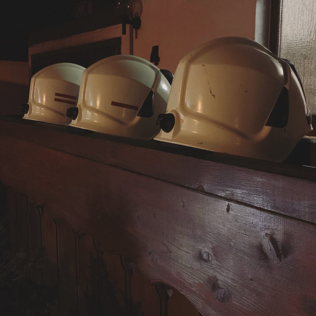 Drei Feuerwehrhelme liegen ordentlich aufgereiht auf einer hölzernen Brüstung im dämmrigen Licht. Die Szene wirkt ruhig und zeigt einen Moment der Pause nach dem Einsatz.
